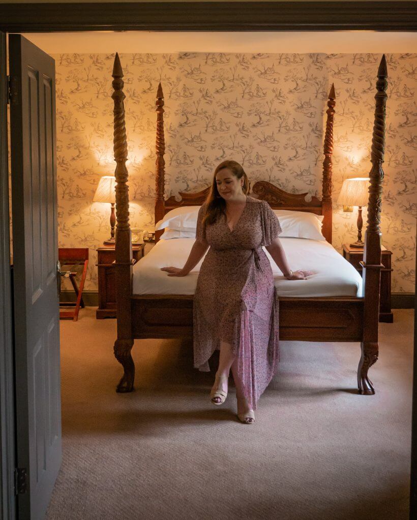 Woman sitting on the bed of a country style four poster bed at Brooklodge Hotel and Macreddin Village