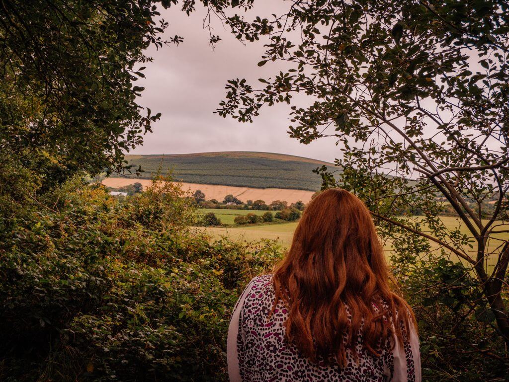 Woman with red hair looking out at a view of the Wicklow mountains from the Railway walk in Tinahely Ireland.
