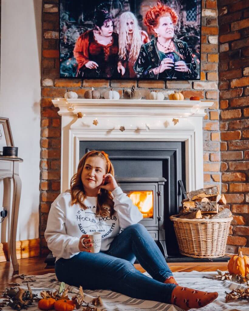 Woman sitting in front of a fire surrounded by pumpkins posing for a Halloween Instagram photo
