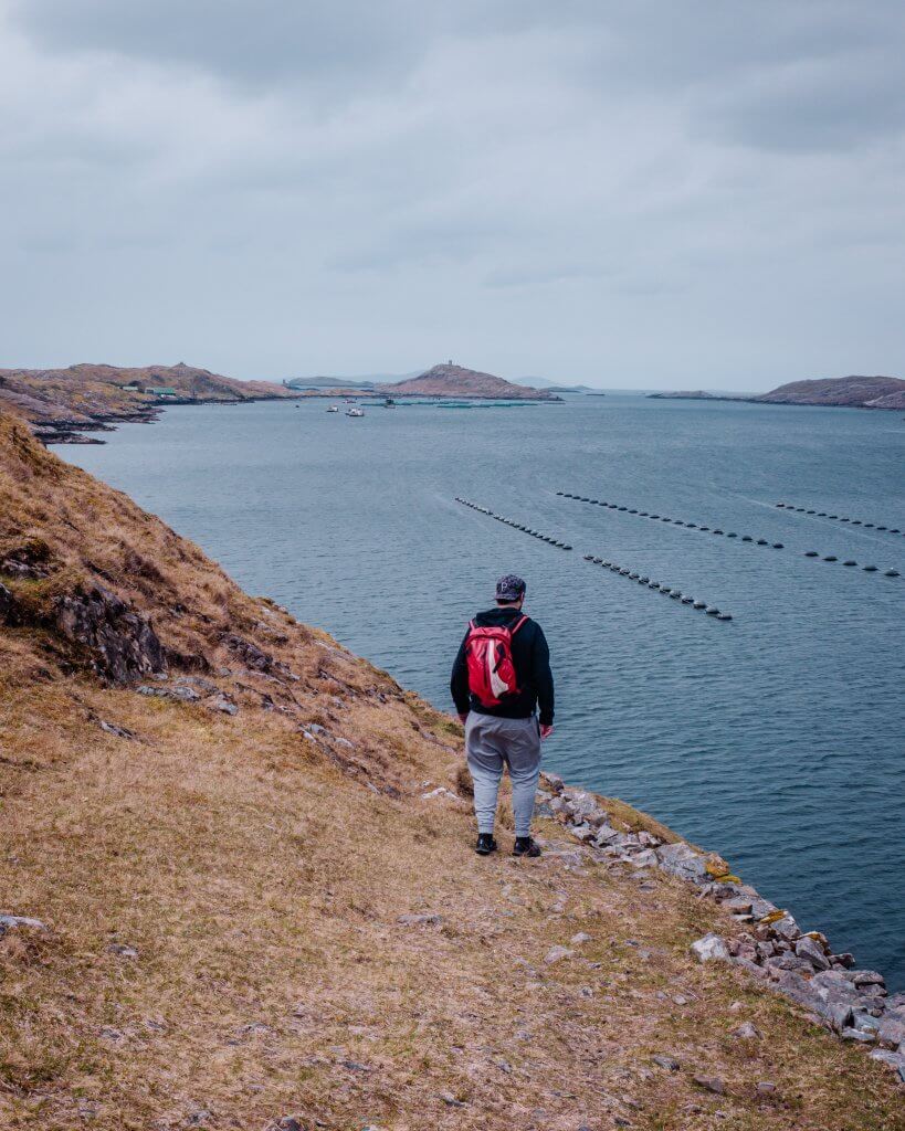 Man in a grey tracksuit and red backpack walking along the edge of Killary Harbour on a Connemara hike