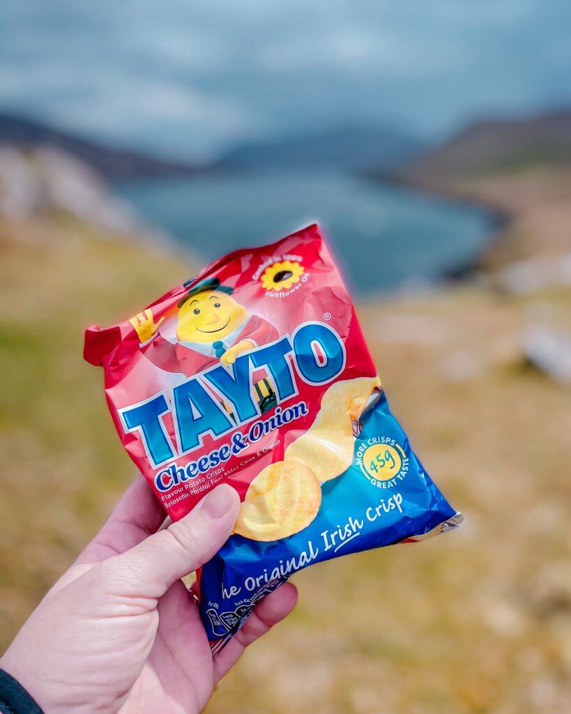 Hand holding up a bag of Tayto on a Connemara hike