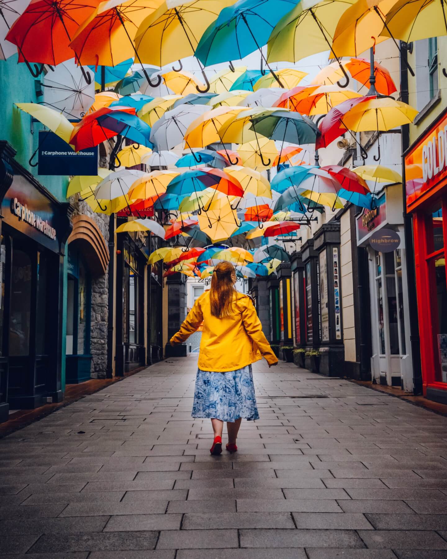 Woman in a yellow raincoat walking under an umbrella sky in the medieval city of Kilkenny