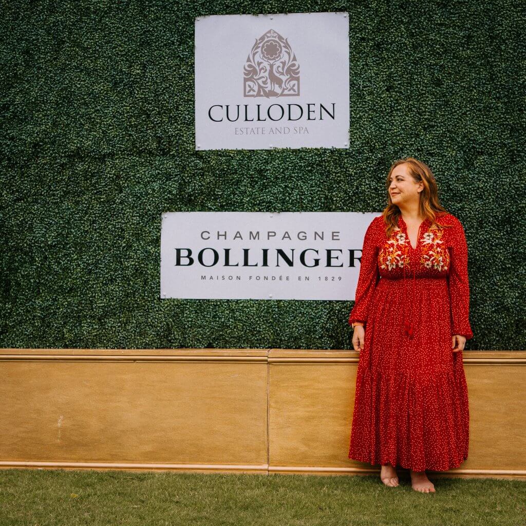 Woman in a red dress standing at a Bollinger Champagne ivy wall at the art & soul art exhibition at Culloden Estate
