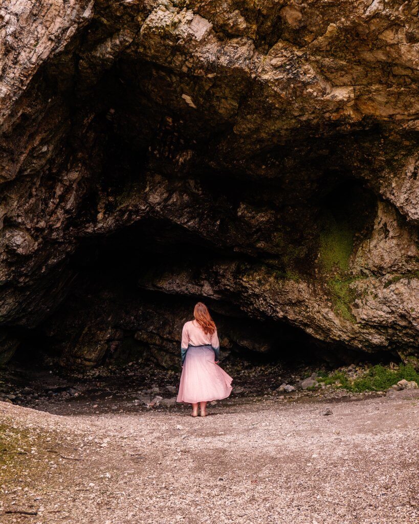 Woman in a pink dress walking into a cave at Ballintoy Harbour where Game of Thrones was filmed
