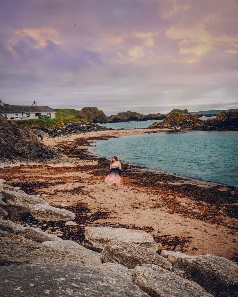 Woman in a pink dress walking barefoot on the beach at Ballintoy Harbour