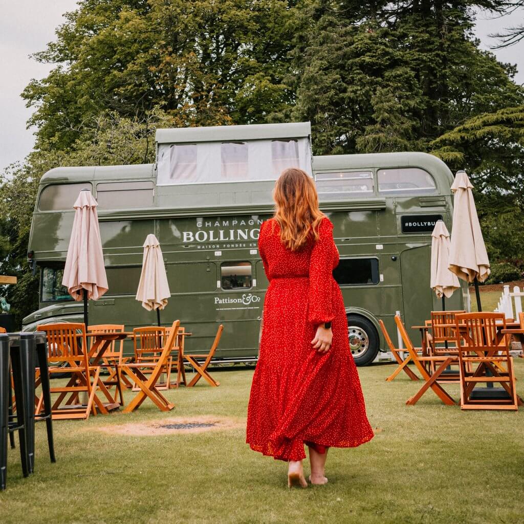 Woman in a red dress walking towards the Bollinger Bus at Culloden Estate to get champagne