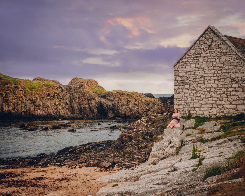 Woman in a pink dress sitting on the rocks at Ballintoy Harbour in County Antrim