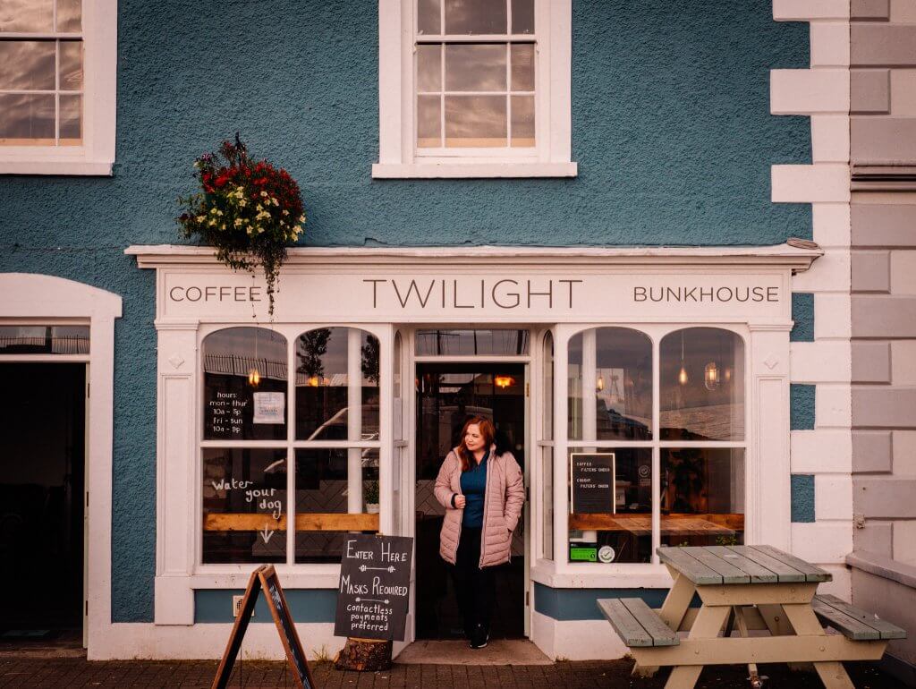 Woman in a pink coat standing in the doorway of Twilight cafe in Carlough Harbour a game of thrones Ireland filming location