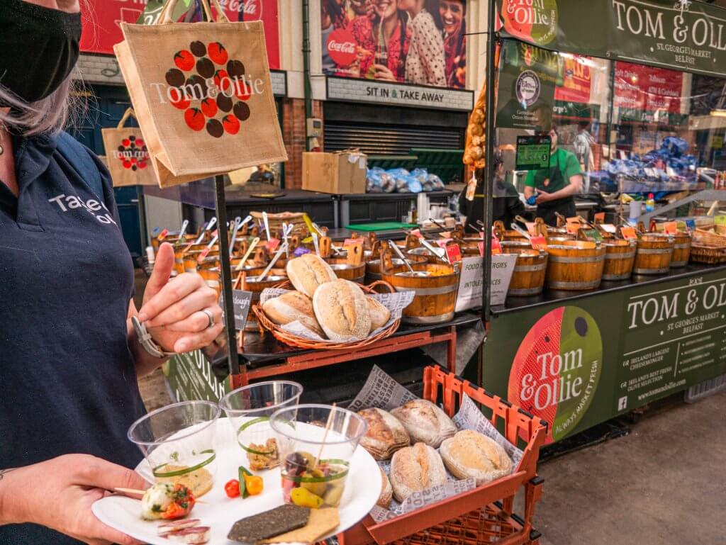 People sampling food at a market stall on a walking tour of Belfast