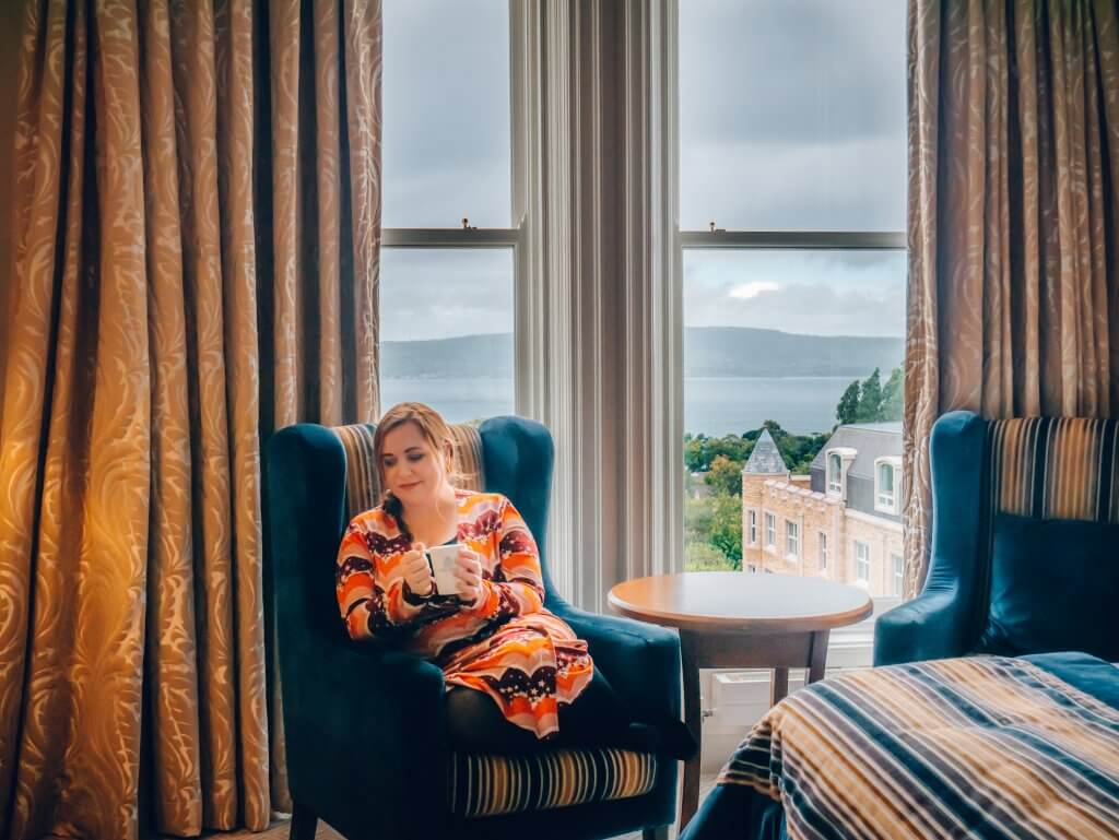 Woman drinking tea in a chair in her hotel bedroom at Culloden Estate