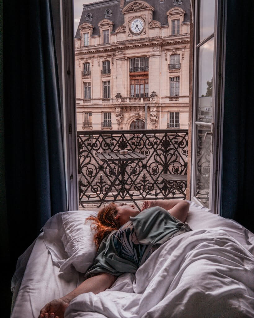 Woman lying in a bed of her hotel room in Bordeaux with a view of Gare St Jean train station 