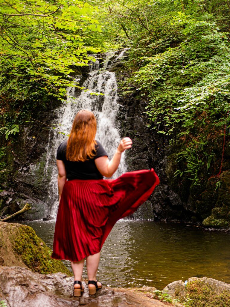 Woman in a red skirt standing in front of Glenoe Waterfall in Antrim Northern Ireland