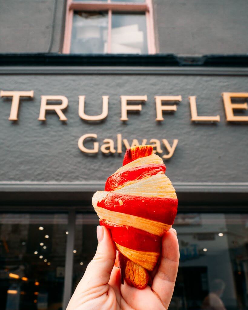Woman holding up a pastry outside Truffle Galway on a Galway Food Tour