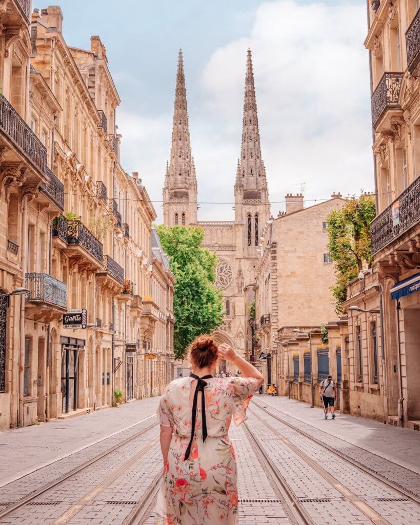 Woman with her back to the camera looking at Bordeaux cathedral from the Gambetta tram stop
