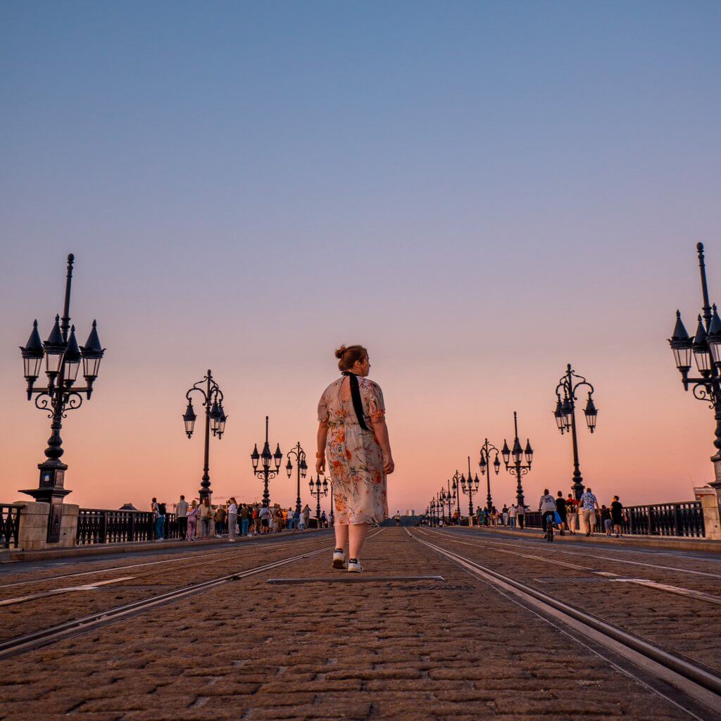 Woman in a floral dress crossing the Pointe de Pierre bridge in Bordeaux at sunset