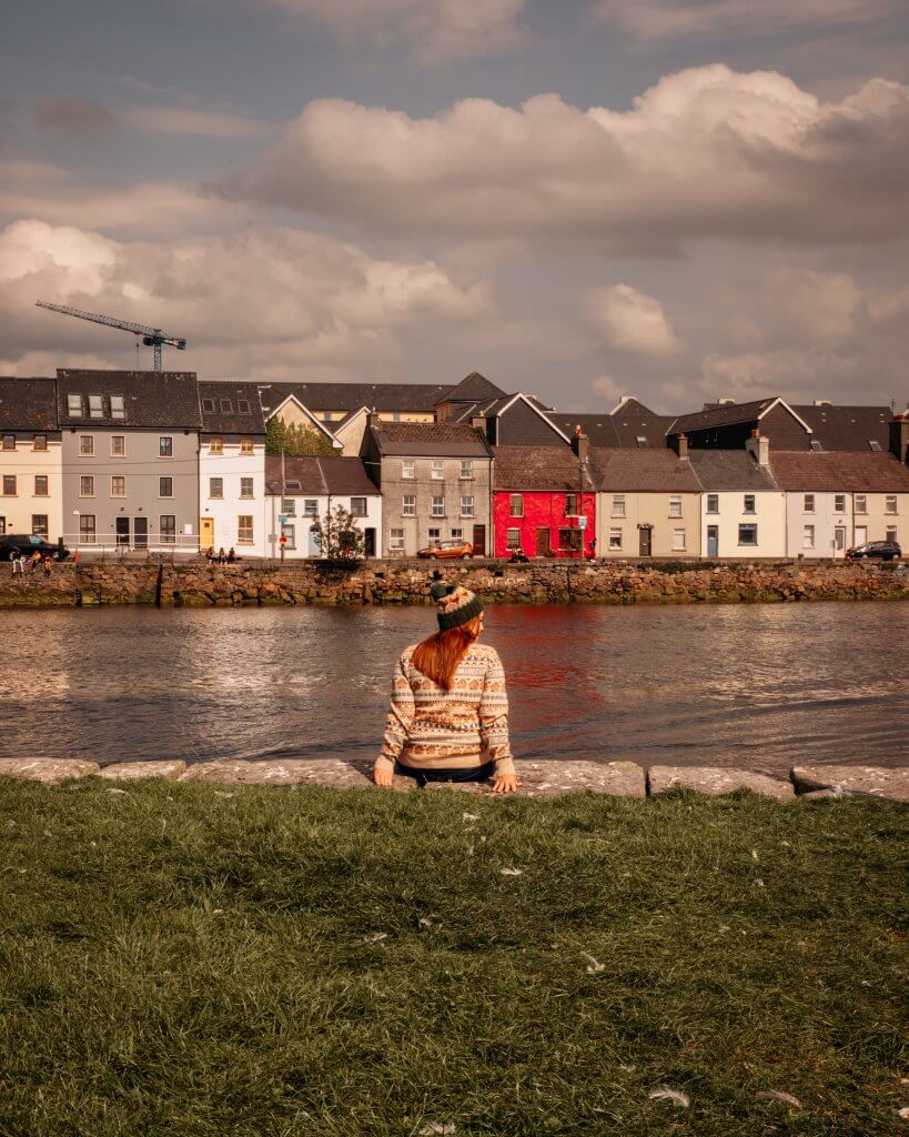 Woman sitting on The Long Walk watching a Galway Hooker on a weekend break in Galway