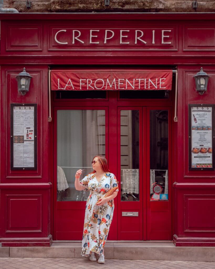 Woman standing outside la fromentine creperie in Bordeaux france with a baguette in her hand