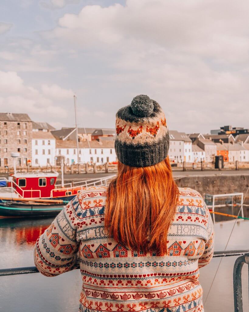 Woman wearing a woolly jumper and hat looking out over Galway Bay