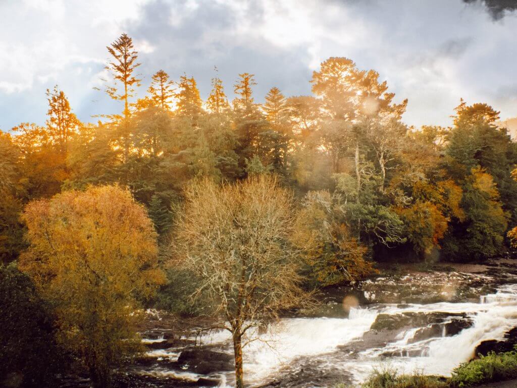 Sunset over Sheen Falls waterfall, painting the sky with hues of orange and pink, creating a magical atmosphere.