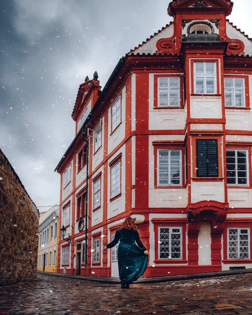 Woman in a green velvet dress walking alongside colourful buildings in Novy Svet Prague