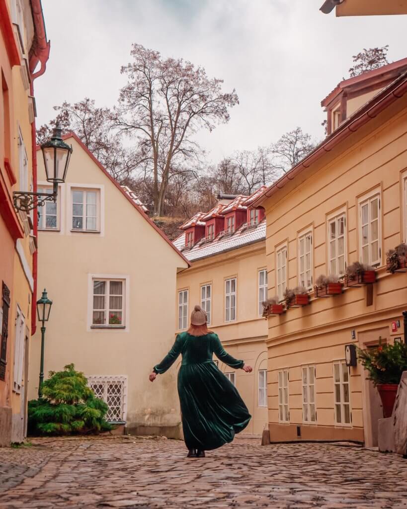 Woman in a long green velvet dress walking along the charming streets of Novy Svet in Prague