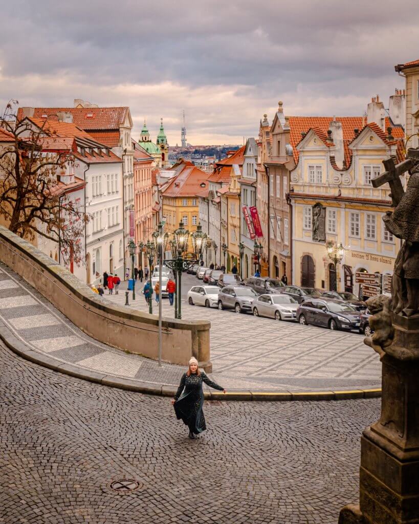 Woman in a green velvet dress twirling at the top of Nerudova street an iconic Instagram spot in Prague