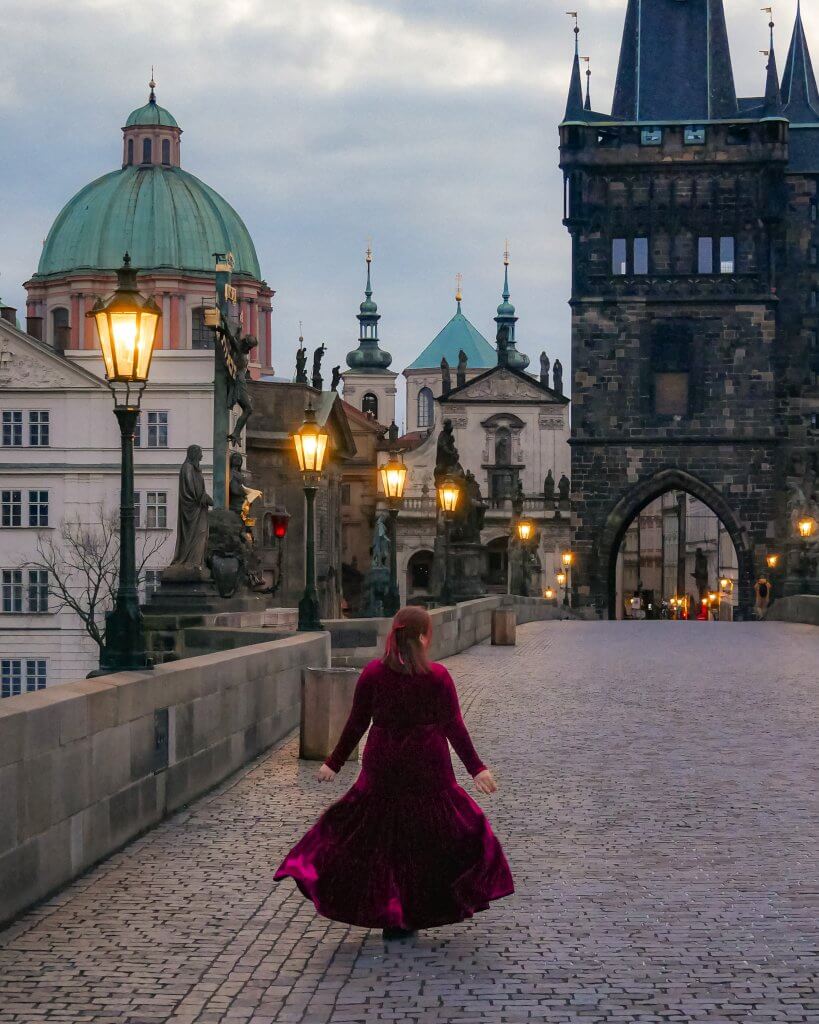 Woman in a long red velvet dress at the gothic Charles Bridge in Prague