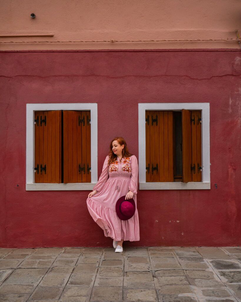 Woman in a pink dress standing beside the colourful houses on Burano Island an Instagram spot that you don't want to miss near Venice