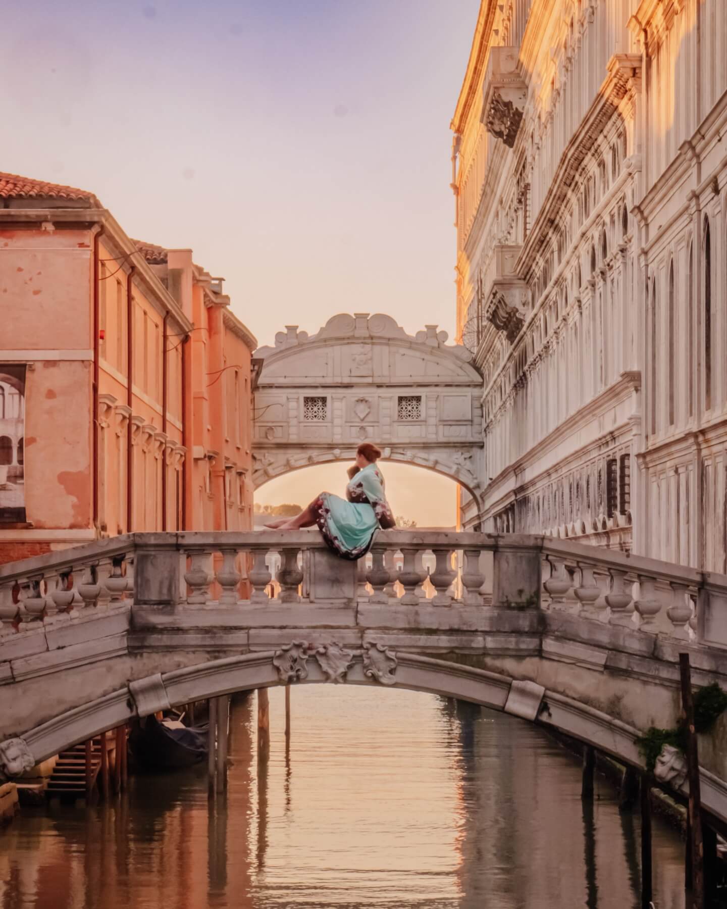 Woman sitting on a bridge in Venice at sunrise. The Bridge of Sighs, one of best Venice Instagram spots