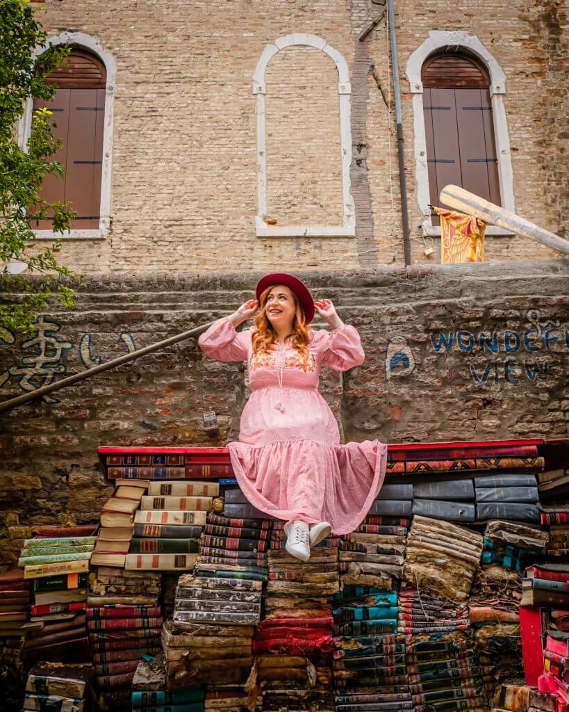 Woman sitting on a platform of books at Libreria Acqua Alta a hidden Venice Instagram spot.
