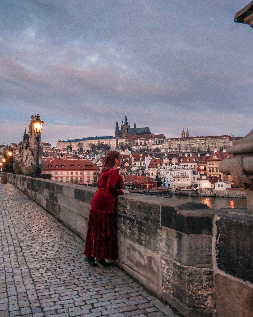 Woman in a long red velvet dress looking over Charles Bridge in Prague at Prague Castle on the hilltop