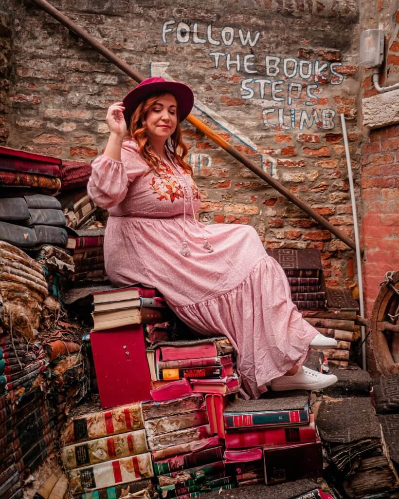 Woman sitting on a staircase made of books at Libreria Acqua Alta a popular Instagram spot in Venice Italy