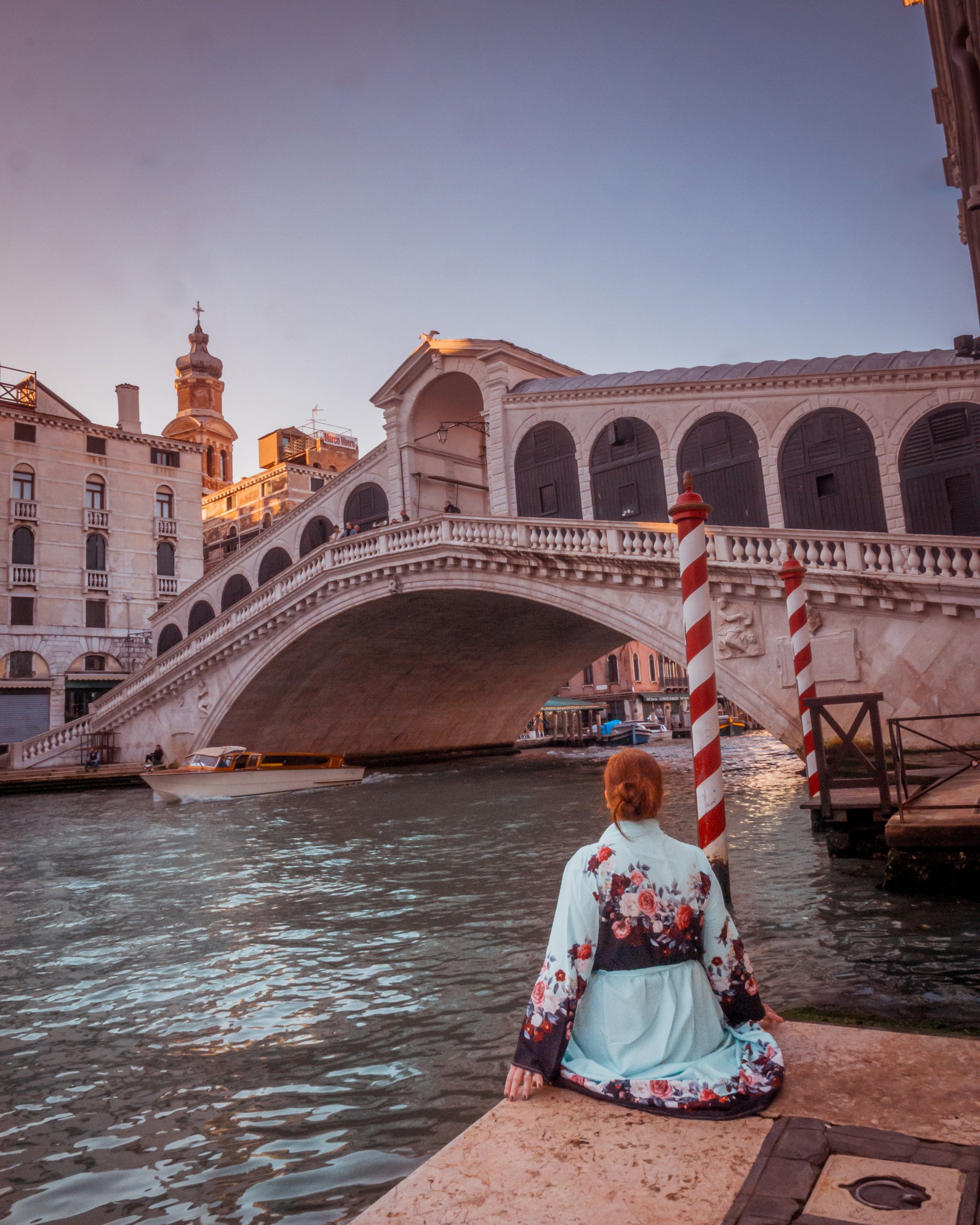 Woman sitting on a dock on the Grand Canal in Venice looking at the Rialto Bridge