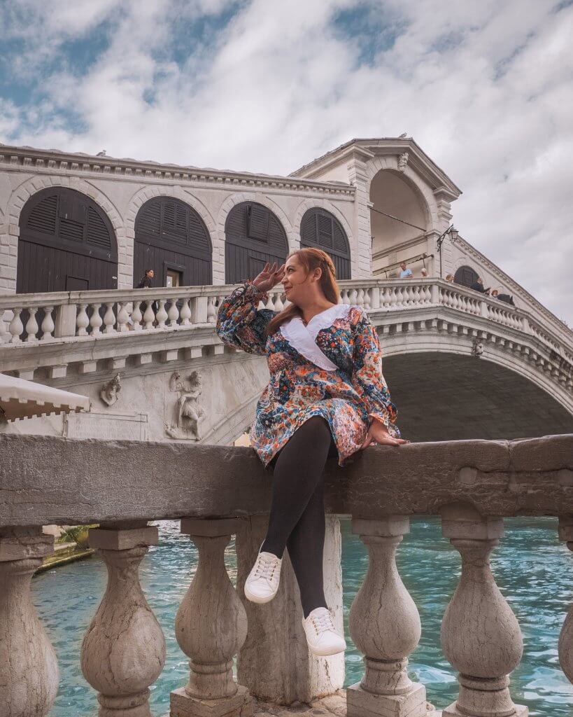 Woman sitting on a terrace with the Rialto Bridge on the Grand Canal of Venice behind here. A great Instagram spot in Venice