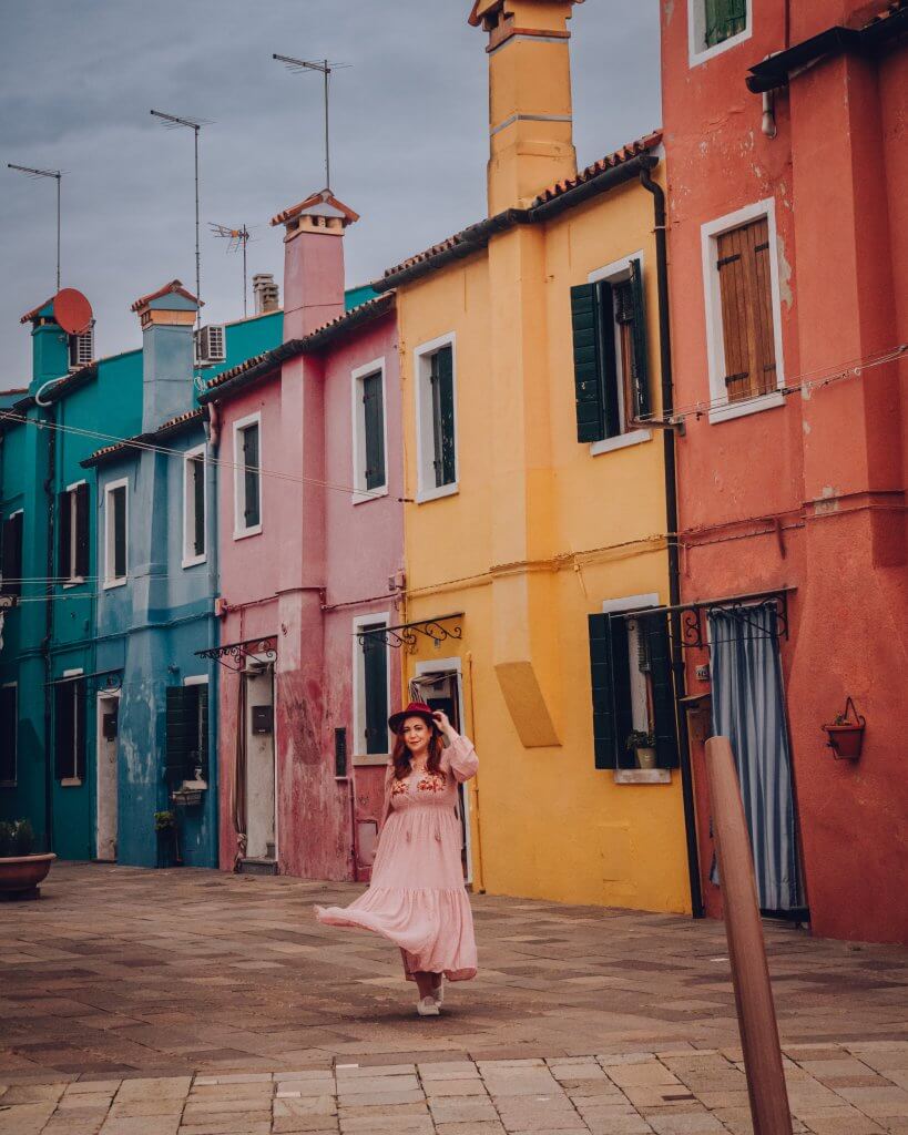 Woman in a pink dress standing beside the colourful houses in Burano Island 