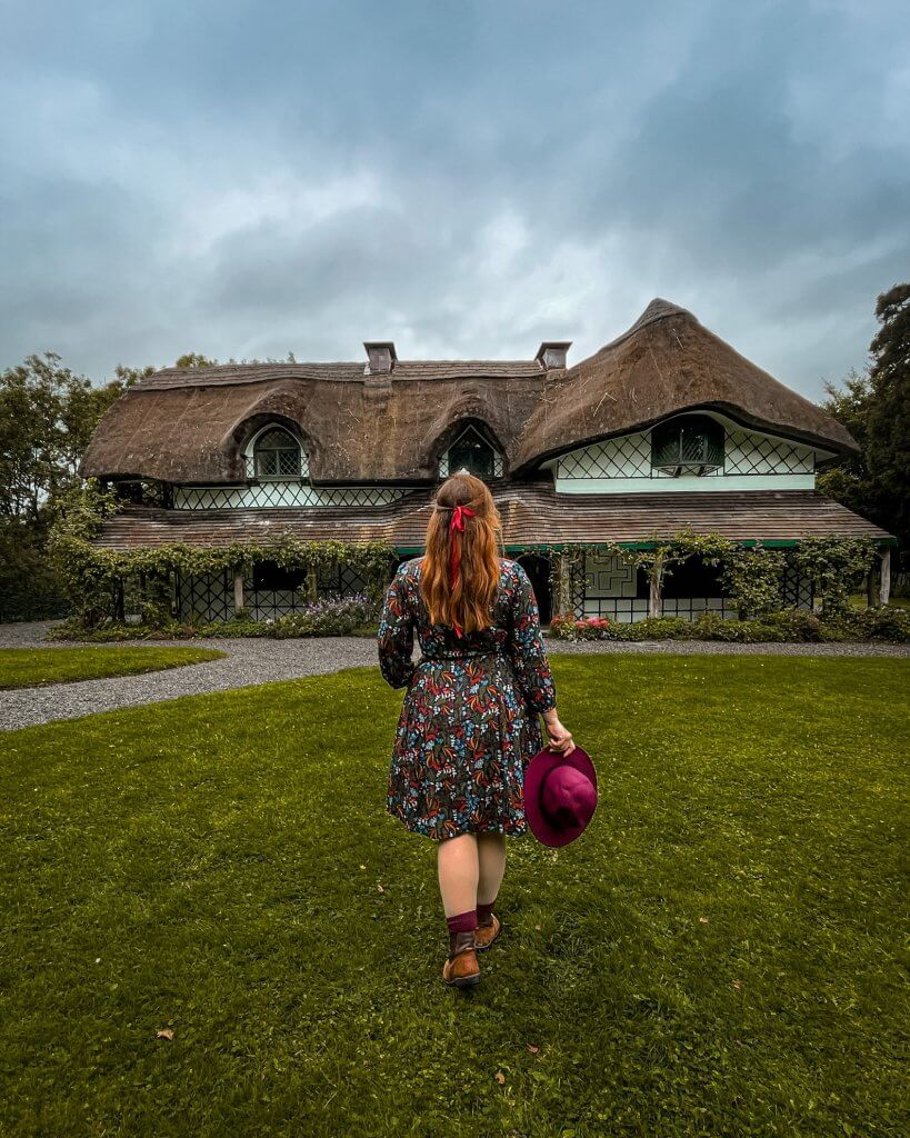Woman in a short dress holding a pink hat walking at the garden of Swiss Cottage Cahir