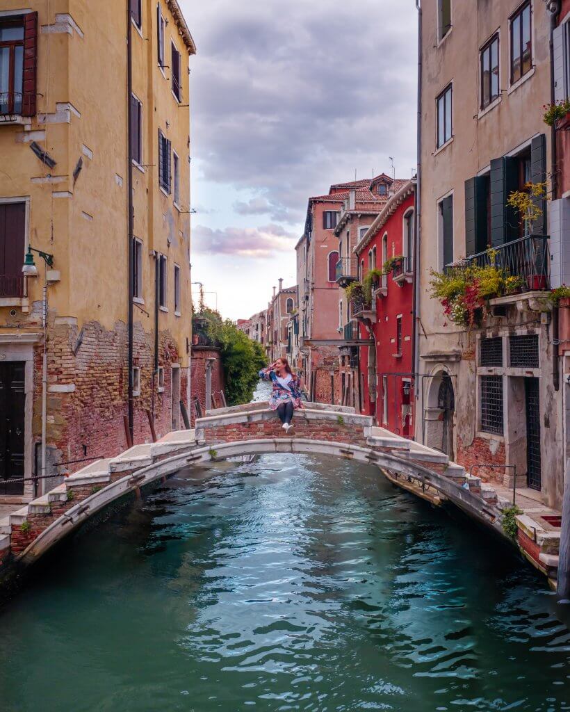 Woman sitting on the Ponte Chiodo bridge without guardrails in Cannaregio Venice Italy one of the best Venice Instagram spots