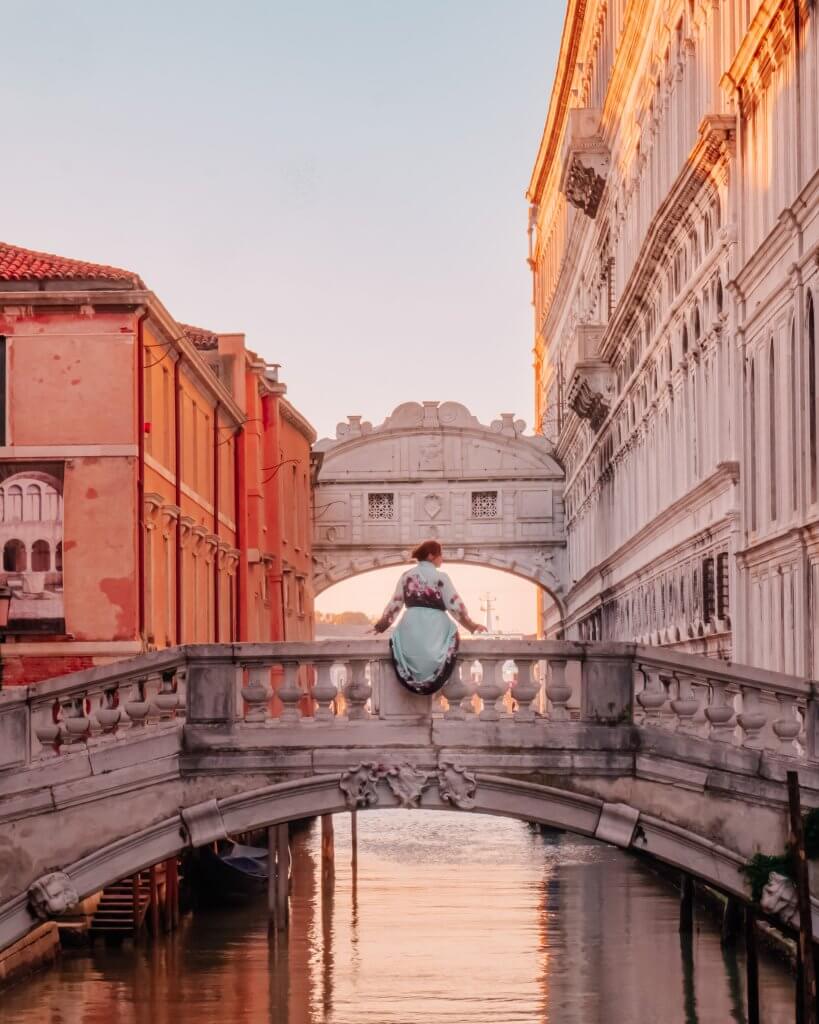 Woman in a blue dress sitting on a bridge in Venice. Watching the Bridge of Sighs at sunset is one of the best things to do in Venice.