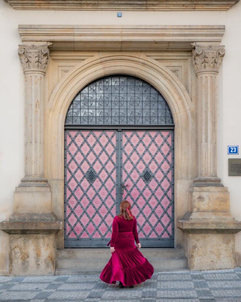 Woman in a red velvet dress standing in front of a pretty door in Prague, the perfect Prague Instagram Spot