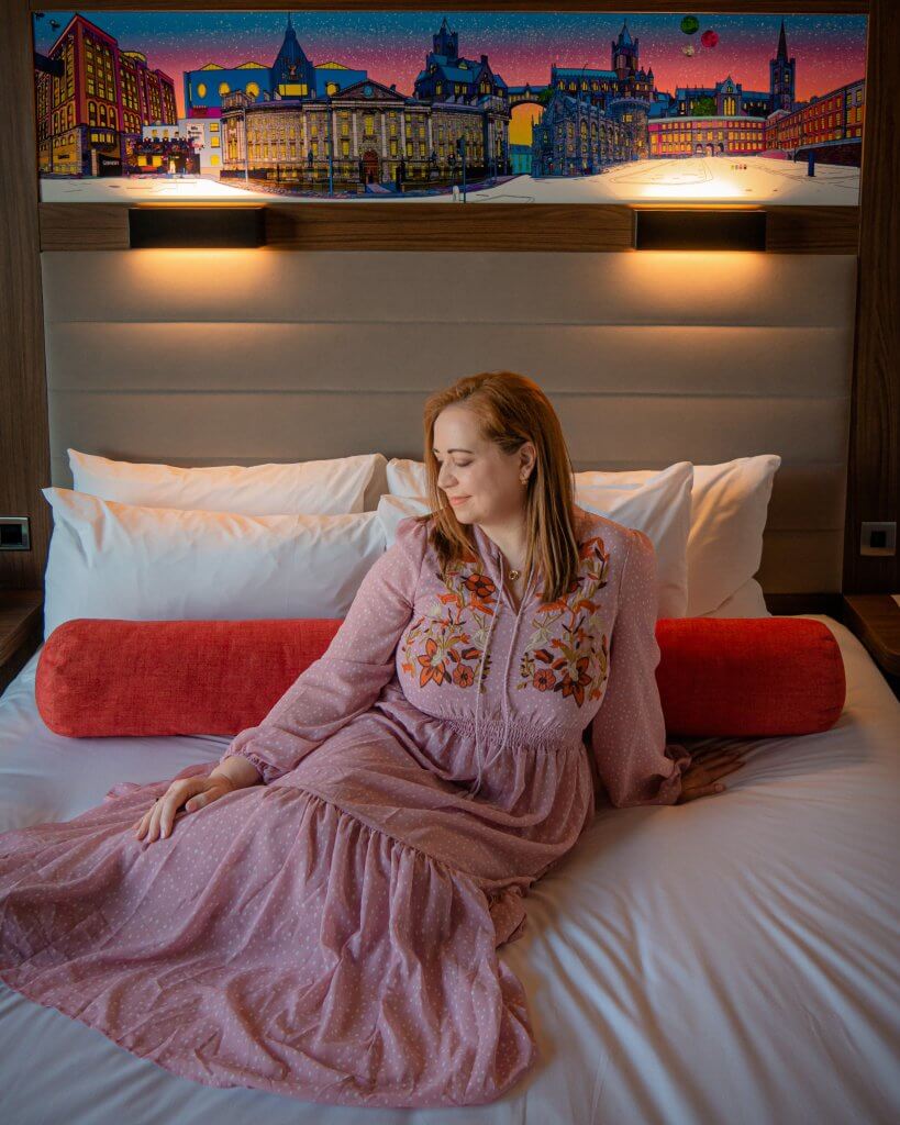 Woman in a pink dress sitting on the bed in Aloft Dublin City Hotel 