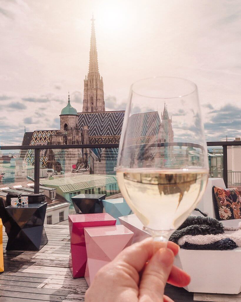 Woman holding a glass of wine to the skyline of Vienna at Lamee Rooftop bar