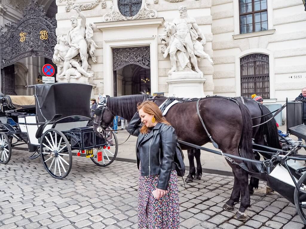 Woman standing in front of a horse and carriage at Hofburg Palace in Vienna, Austria