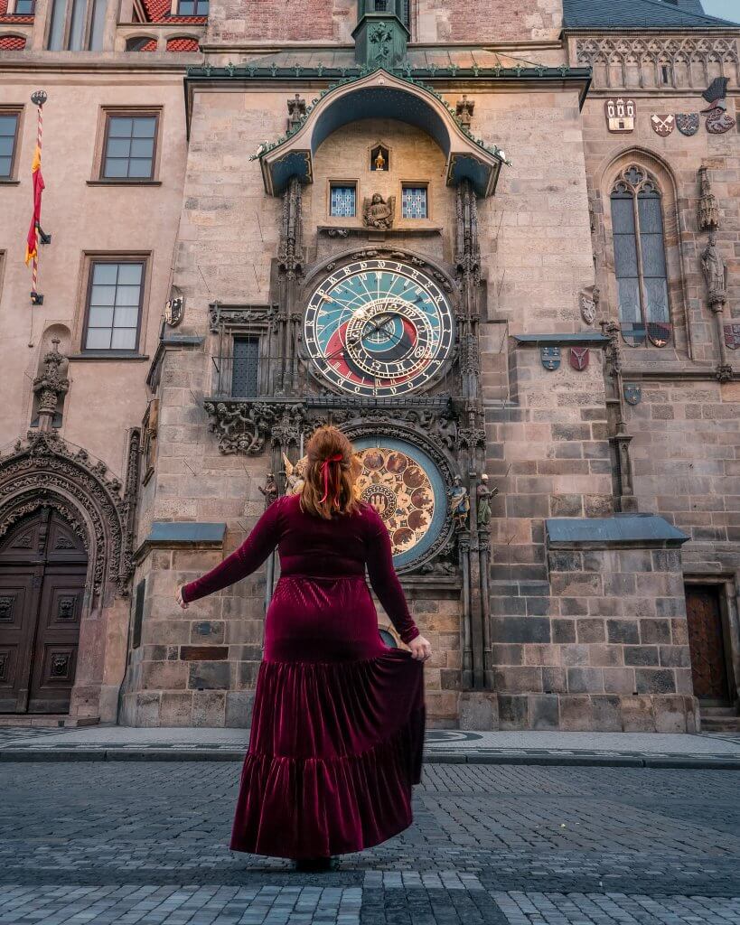 Woman in a red velvet dress looking up at the astronomical clock in Prague during a 2 day prague itinerary