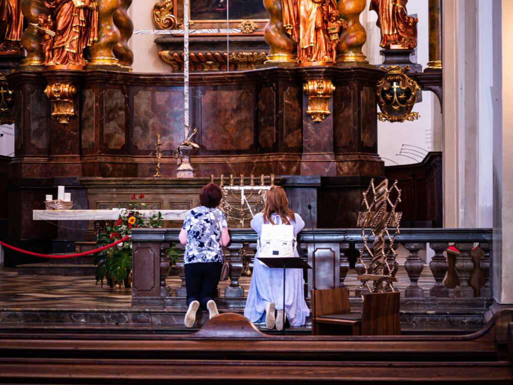 Mother and daughter in law kneeling at the altar of the church of our lady of victories while visiting the child of Prague