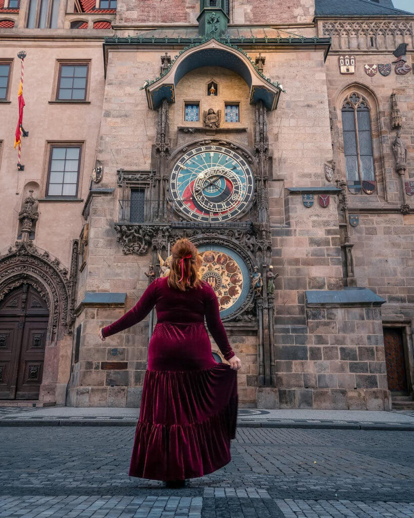 Woman in a red velvet dress standing at the astronomical clock in Prague city a hidden gem in Europe on a small group tour of europe
