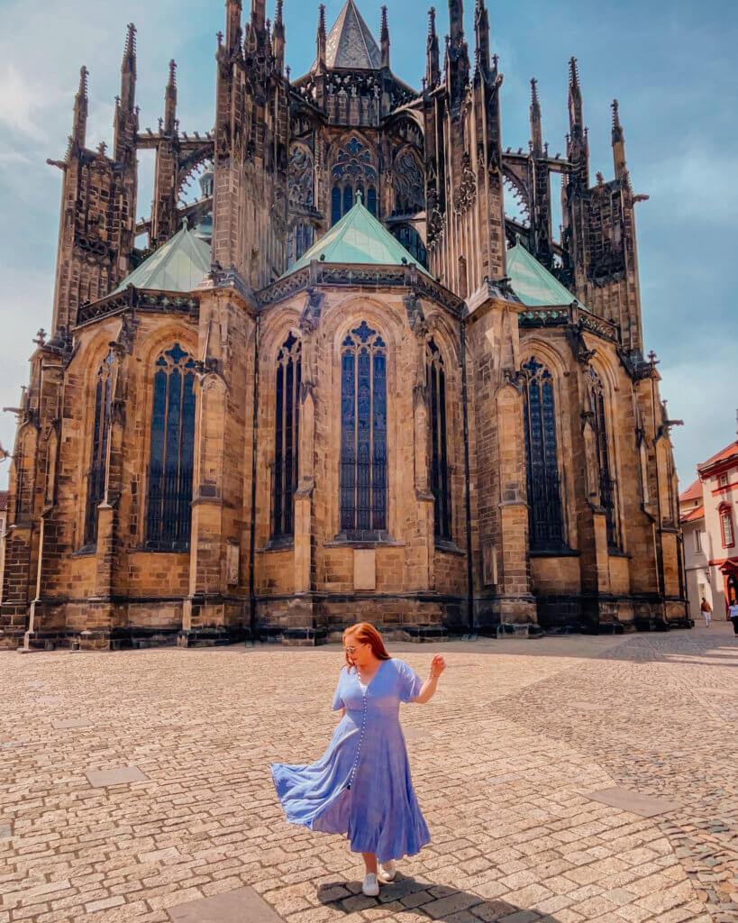 Woman in a blue dress twirling in front of St Vitus cathedral in Prague