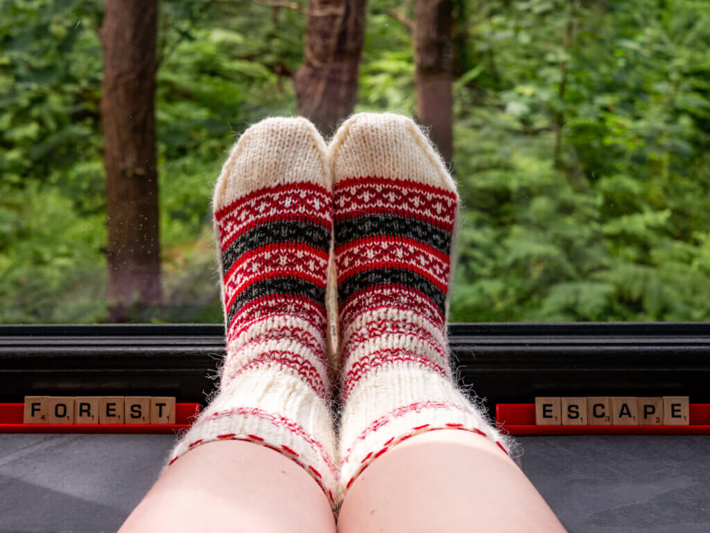 Feet wearing hand knit woollen socks against a forest backdrop