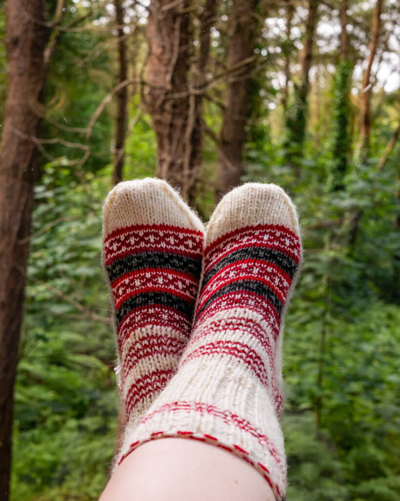 Woman's feet wearing handknit colourful socks against a forest backdrop