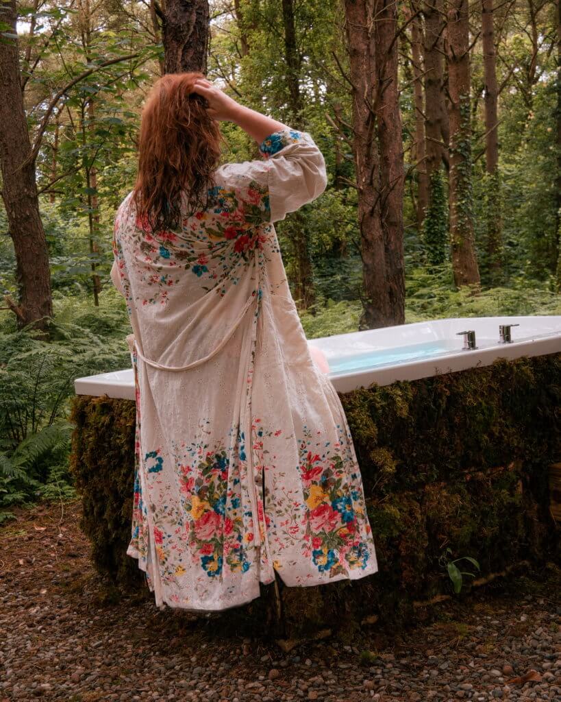 Woman in a floral robe sitting on the edge of an al fresco whirlpool bath in Burrenmore Nest in Northern Ireland