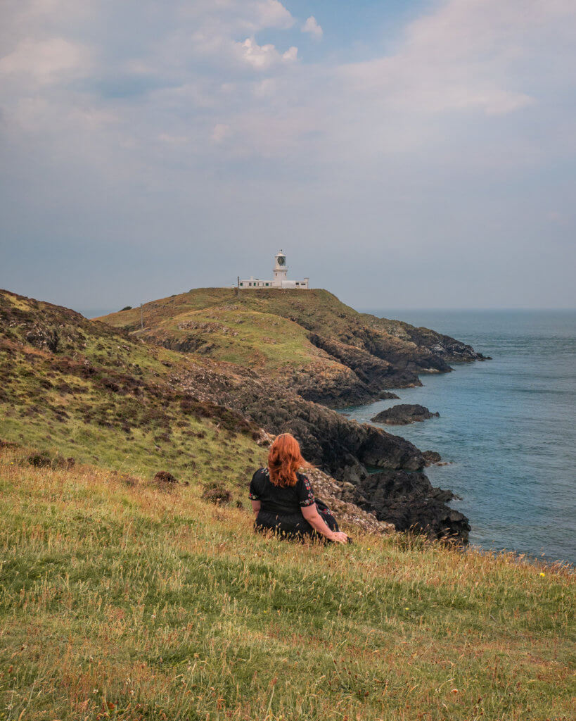 Woman with red hair sitting at Strumble Head Lighthouse in Wales